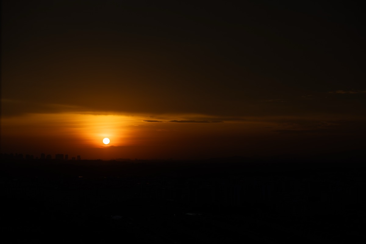 The sun sets in a golden haze over a distant city skyline.