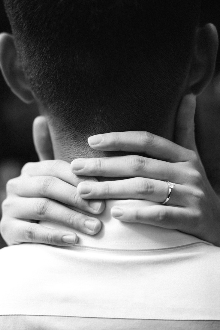 Black-and-white close-up of a couple's hands clasped at the nape of a neck, a new ring on her finger.