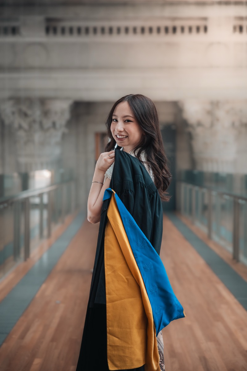A graduate turns to smile, her gown slung over one shoulder.