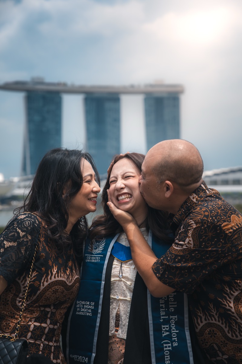 Family share a kiss on the cheek, Marina Bay Sands behind them.