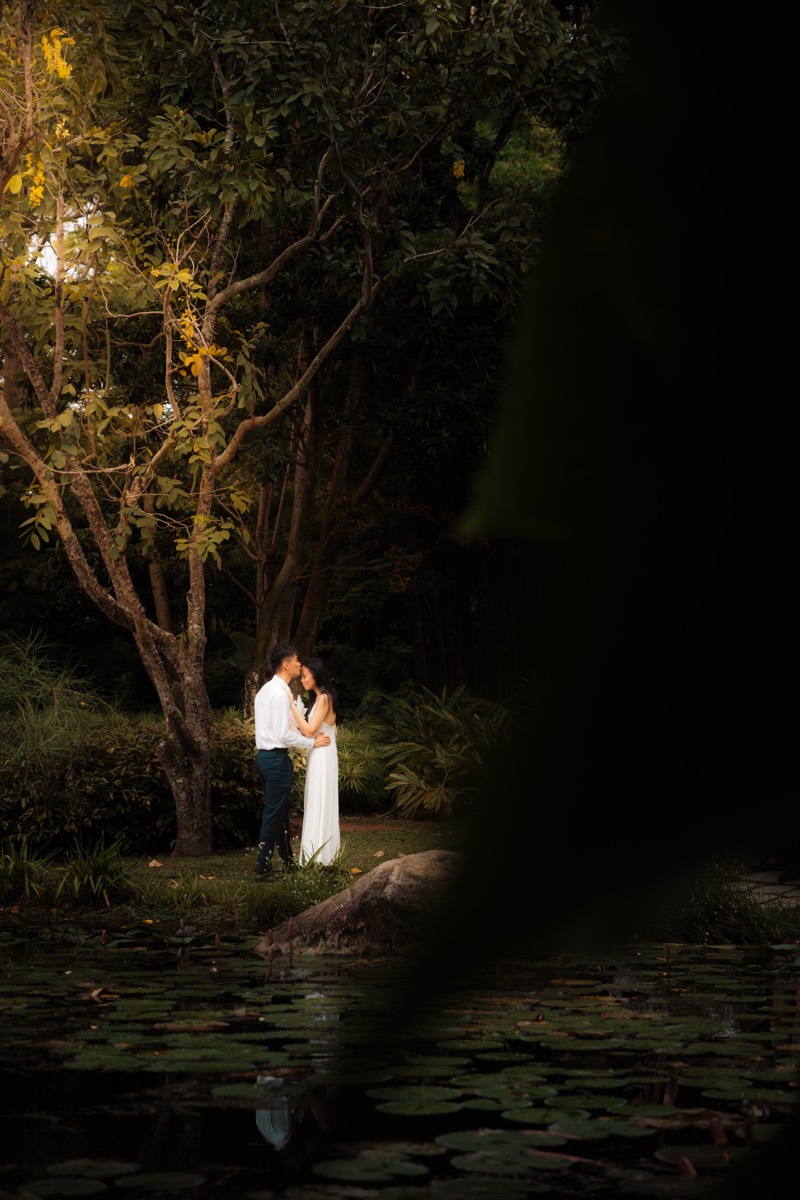 A couple stand close at a still lily pond in the last blue light.