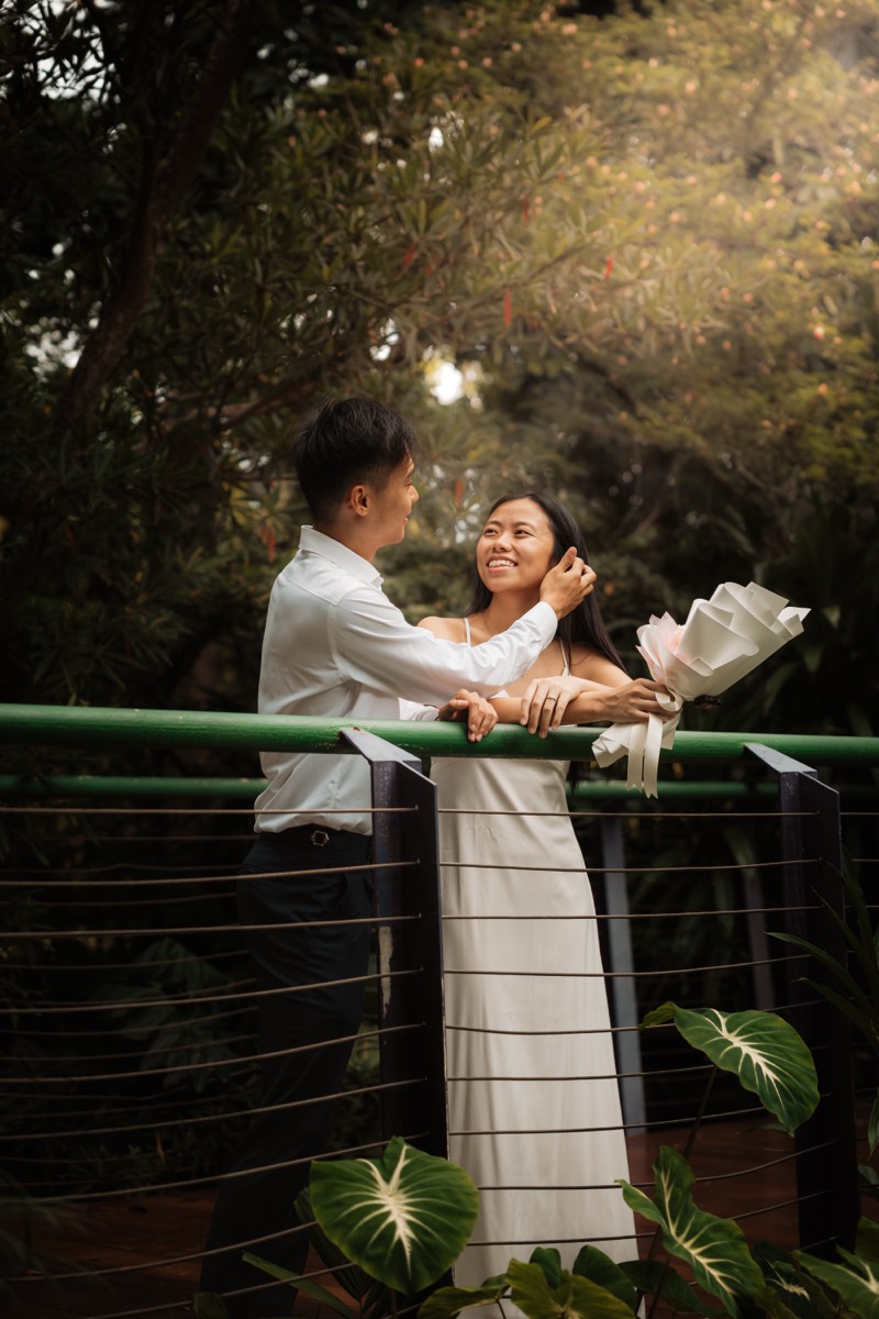 The couple lean on a garden railing surrounded by greenery.