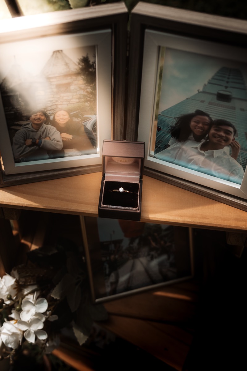 An engagement ring in its box, propped beside framed photos of the couple.