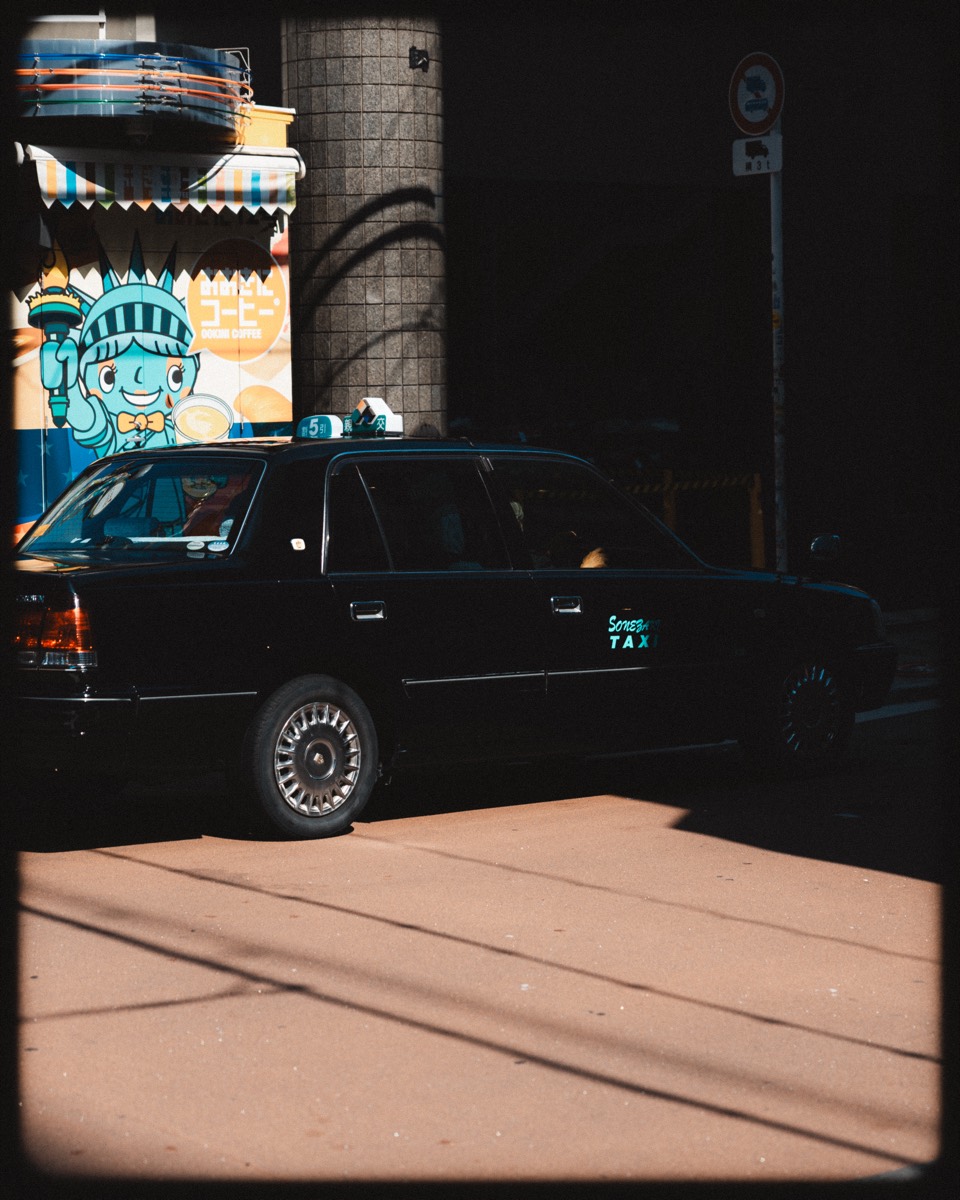 A black taxi caught in hard afternoon light and deep shadow.
