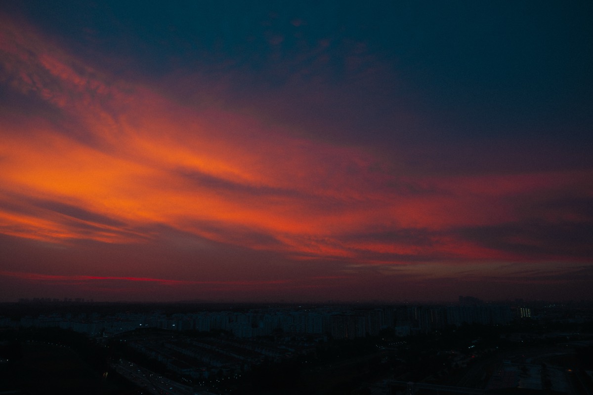 Bands of orange and blue cloud burn over a darkening city skyline at dusk.