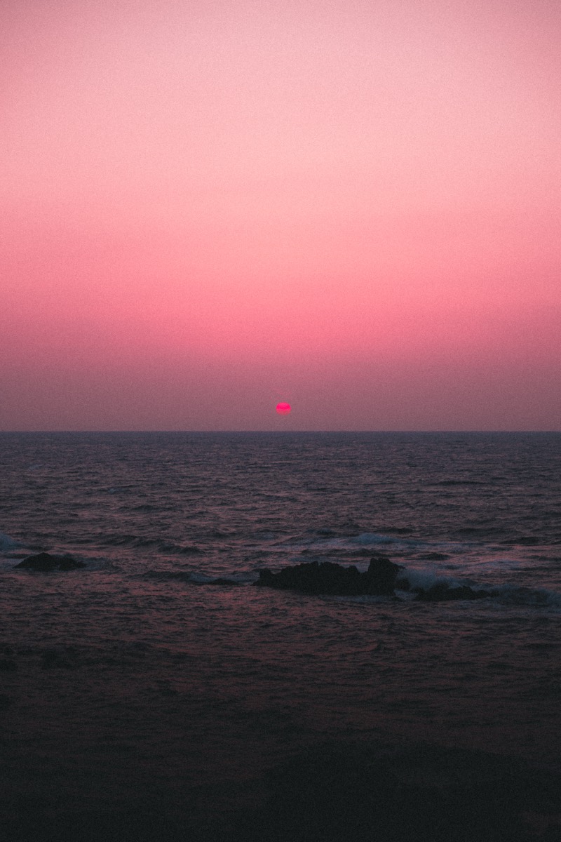 A small sun sinks into a rose-coloured sea and sky.