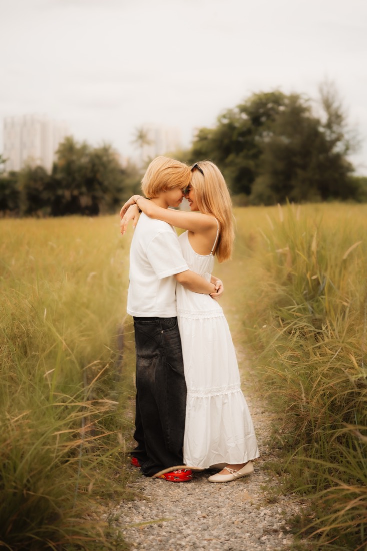 A couple hold each other forehead to forehead on a quiet path through tall grass.