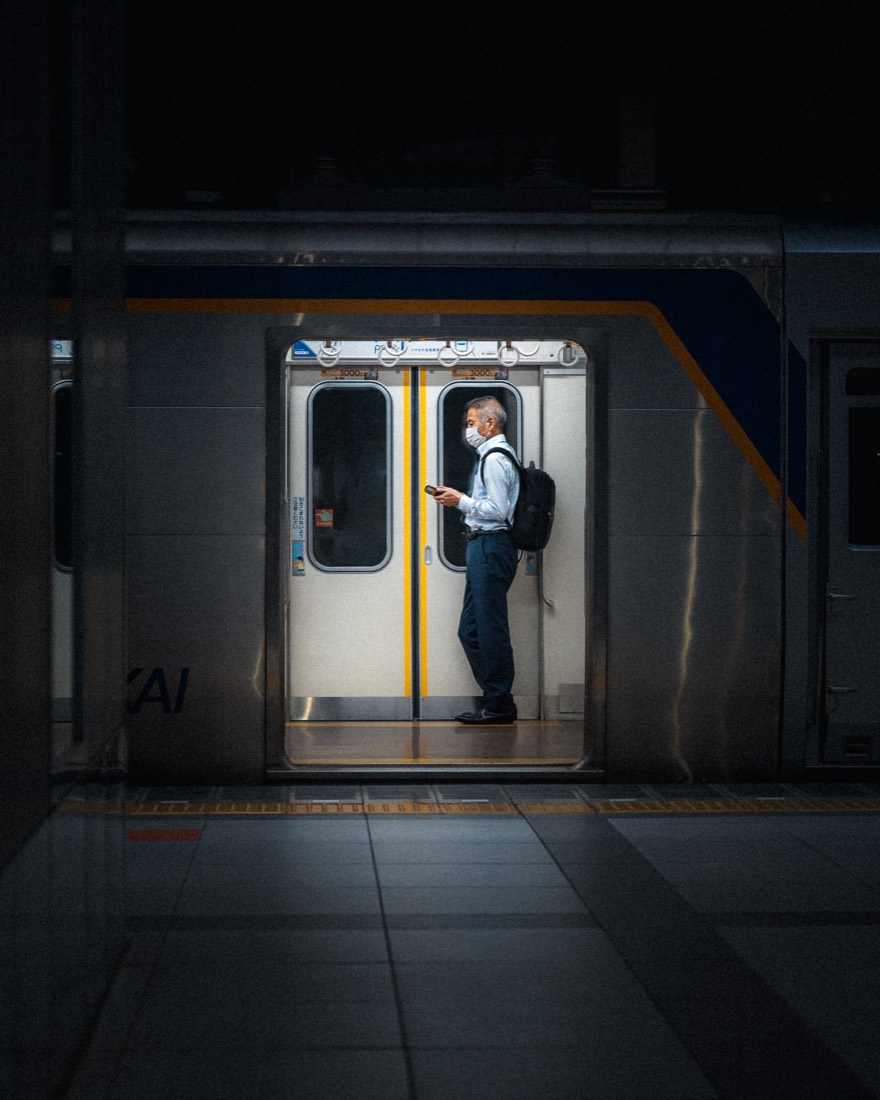 A commuter stands framed in the open doorway of a train, lit cool against the dark platform.